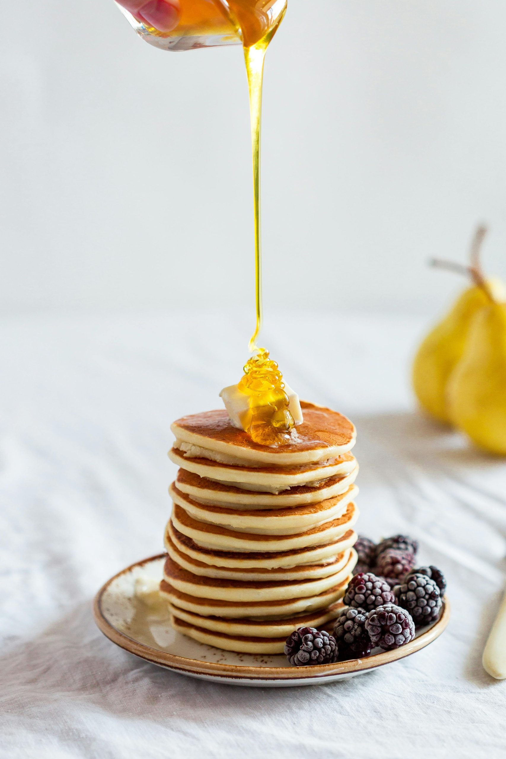 Mouthwatering stack of pancakes drizzled with honey, garnished with blackberries.