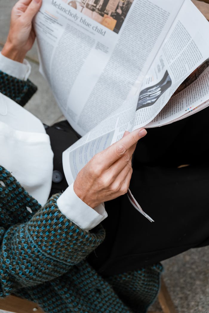 A woman in stylish attire reads a newspaper outdoors, embodying elegance and modernity.